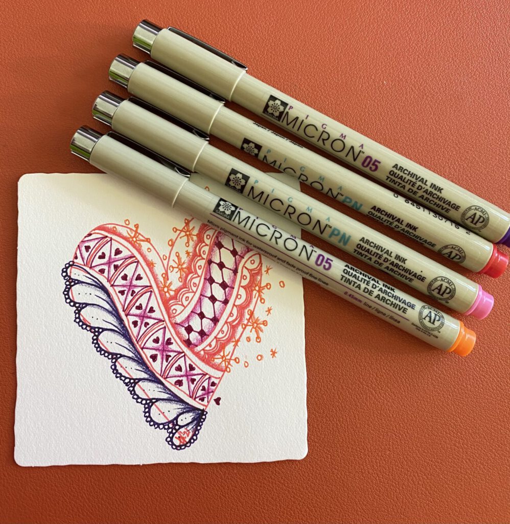 A Zentangle heart drawn in pink and purple ink, with Micron pens beside it